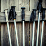 An image of six aluminum ski poles, which are a type of recyclable ski pole shaft, leaning against a wooden fence,